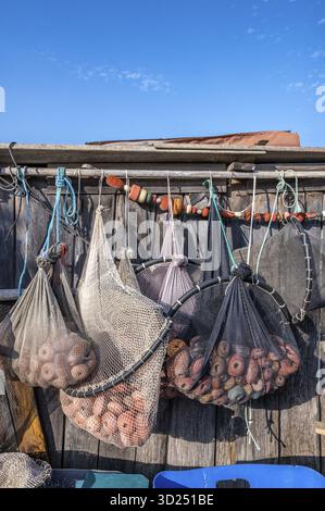 Nahaufnahme verschiedener Fischernetze und Fallen mit roten Schwimmern und Fesseln, die zum Trocknen an einer rauen Holzwand eines Fischerhauses in der hängen Stockfoto