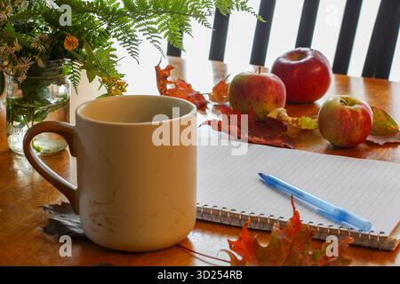 Gemütliche Herbstszene mit Notizbuch, Kaffeetasse, Äpfeln und bunten Herbstblättern Stockfoto