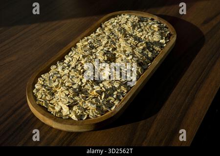 Holzschale mit Haferflocken, fotografiert in warmem Sonnenlicht aus der Seitenperspektive auf dunklem Holztisch. Stockfoto