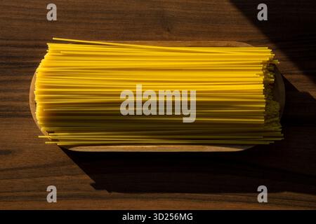 Ungekochte Spaghetti-Pasta in Holzschale auf dunklem Tisch mit Sonnenlicht und Schatten. Stockfoto