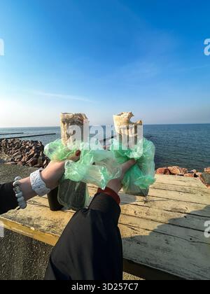 Die Hand der Person hält die Kebab-Folie. Beliebtes Street Food. Meer im Hintergrund. Essen mit Aussicht. Stockfoto