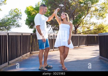 Ein lächelndes Paar tanzt draußen, ein Mann, der eine Frau hält, ist Hand auf einem sonnigen Holzsteg Stockfoto