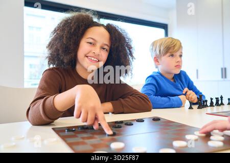 Zwei Kinder sitzen an einem Tisch, eines lächelt und zeigt, während das andere zusieht, als Teil einer pädiatrischen Therapie- und Rehabilitationssitzung, die sich auf Mo konzentriert Stockfoto