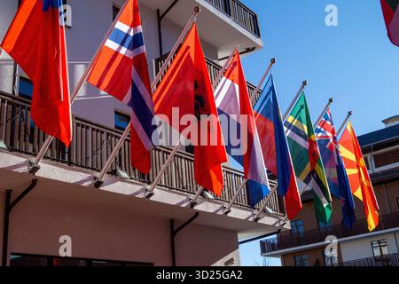 Helle Flaggen aus mehreren Nationen hängen von einem Balkon in einem klaren blauen Himmel. Die Szene zeigt farbenfrohe Banner, die sanft in der leichten Brise, Crea, winken Stockfoto