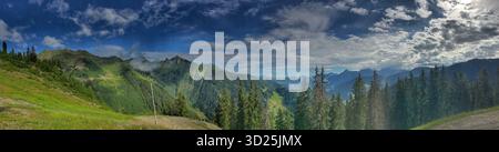 Wunderschönes Bergpanorama mit dichten grünen Wäldern, dramatischen Gipfeln und einem dynamischen bewölkten Himmel. Stockfoto