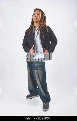Junger Mann mit Dreadlocks und Baggy Jeans posiert selbstbewusst in einem Studio Stockfoto