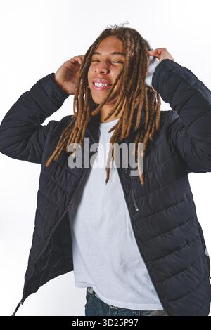 Lächelnder junger Mann mit Dreadlocks, der Audio genießt, Kopfhörer und eine schwarze Jacke trägt Stockfoto