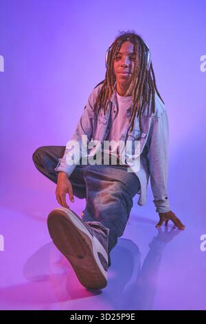 Junger Mann mit Dreadlocks, der Musik über Kopfhörer im neonbeleuchteten Studio hört Stockfoto