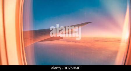 Herrlicher Blick auf den Sonnenuntergang über dem Flugzeugflügel durch Fenster gesehen, farbenfroher Himmel und Wolken, entspannendes Reise- und Tourismuskonzept für Urlaub, Flug, Luft Stockfoto