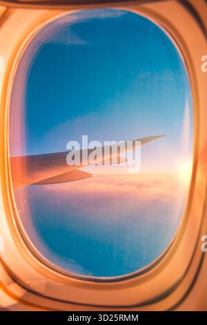 Herrlicher Blick auf den Sonnenuntergang über dem Flugzeugflügel durch Fenster gesehen, farbenfroher Himmel und Wolken, entspannendes Reise- und Tourismuskonzept für Urlaub, Flug, Luft Stockfoto