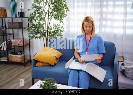 Ernsthafte Ärztin in blauer Uniform, die zu Hause Krankenakten liest Stockfoto