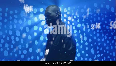 Stehender Mann in dunkler Jacke in dunklem Studio, mit blauen Bokeh-Lichtern und numerischen Projektionen Stockfoto