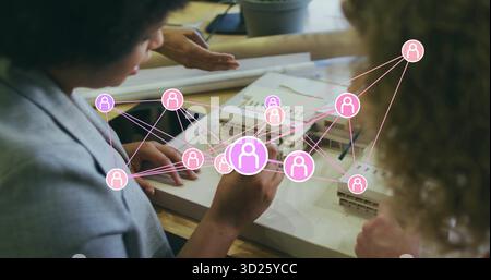 Gruppe von vier Architekten, die maßstabsgetreue Modelle und Pläne im Studio untersuchen, mit pinkfarbenen Netzwerksymbolen und Tablet Stockfoto