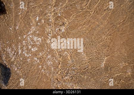 Sonnenlichtreflektionen auf klarem, seichten Meerwasser über Sandstrand Stockfoto