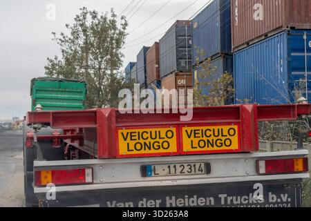 Rückansicht des Lkw-Anhängers mit Veiculo longo-Schild in der Nähe von gestapelten Versandcontainern Stockfoto