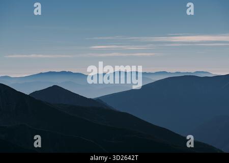 Ein atemberaubender Blick auf mehrschichtige Bergkämme, die in die Ferne gleiten, umhüllt von weichem Nebel unter einem ruhigen Abendhimmel. Die beschauliche Szene einfängt Stockfoto
