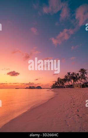 Friedlicher tropischer Sonnenuntergangsstrand mit Palmensilhouetten, romantischem Himmel und herrlichem Meerblick auf die paradiesische Insellandschaft Stockfoto