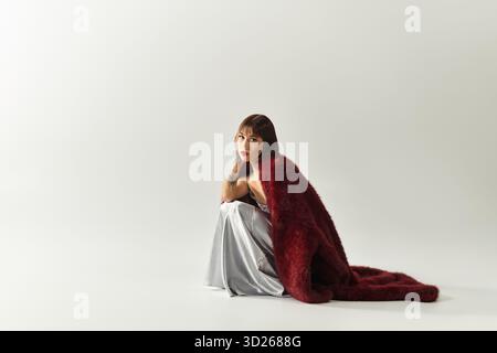 Eine schöne junge Frau sitzt anmutig in stilvoller Kleidung, strahlt Charme und Selbstvertrauen aus. Stockfoto