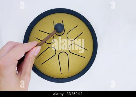 Nahaufnahme einer Hand, die mit einem Gummihammer auf eine goldene Zungentrommel schlägt. Themen wie Achtsamkeit, Klangheilung und musikalische Einfachheit. Wellness, Meditati Stockfoto