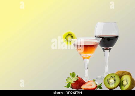 Ein erfrischender Erdbeer-Kiwi-Cocktail, serviert in einem Martini-Glas mit Kiwigarnitur, gepaart mit einem Glas Rotwein, umgeben von frischen Erdbeeren A Stockfoto