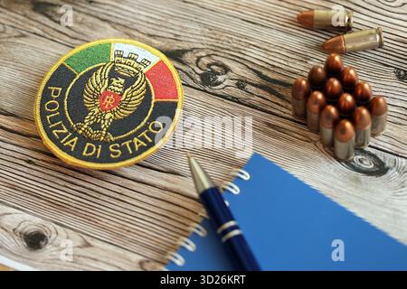 KIEW, UKRAINE - 6. SEPTEMBER 2025 Flicken der italienischen Staatspolizei mit Kugeln und Notizblock auf Holztisch Nahaufnahme Stockfoto