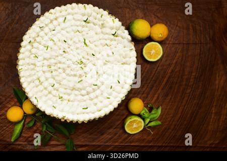Hausgemachte Zitronenkuchen auf einem Glaskuchenständer, dekoriert mit Schlagsahne und Limettenschale. Ein Stück des cremigen Desserts wird auf einem weißen Teller serviert Stockfoto