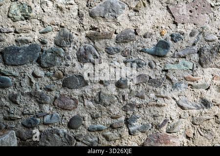 Eine alte Mauer aus Steinen und Kieselsteinen. Die Wand ist grau und hat eine raue Textur Stockfoto