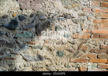 Eine alte Mauer aus Ziegeln und Steinen mit einem Schatten darauf. Die Wand scheint alt und abgenutzt zu sein, wobei einige der Steine fehlen oder abgesplitzt sind Stockfoto