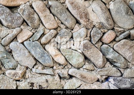 Eine Wand aus Felsen mit einem Zickzackmuster. Die Wand besteht aus großen Felsen und hat eine raue Textur Stockfoto