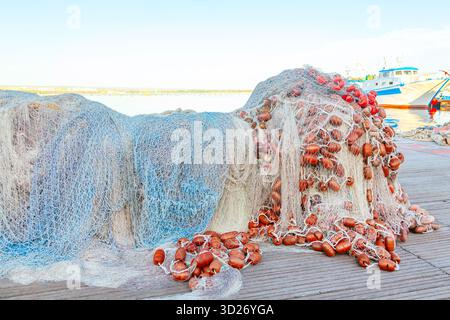 Ein großer Stapel von Fischernetzen mit Schwimmern liegt auf einem Holzsteg gesammelt. Stockfoto