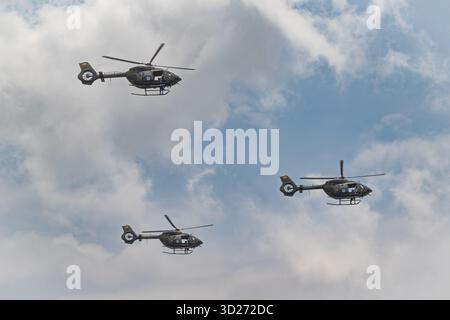 Drei dunkle Militärhubschrauber der ecuadorianischen Luftwaffe fliegen in präziser Formation gegen einen blauen und bewölkten Himmel. Stockfoto