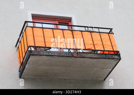 Flacher Blick auf einen Vintage-Balkon mit orangefarbenem Stoff auf einem schwarzen Eisengeländer. Stockfoto