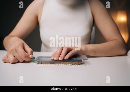 Nahaufnahme einer Frau, die den Displayschutz an einem modernen Smartphone anbringt, um eine präzise Ausrichtung zu gewährleisten und optimalen Schutz vor Kratzern und Potenzial zu gewährleisten Stockfoto
