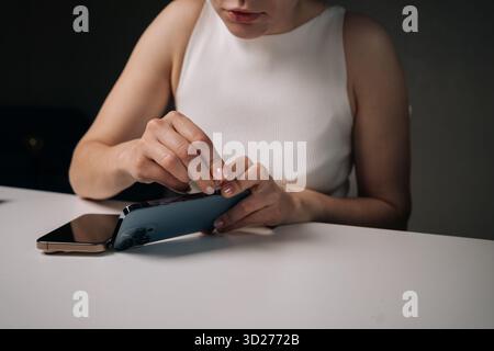 Zugeschnittene Aufnahme einer Frau, die an einem weißen Tisch sitzt und das sim-Auswerferwerkzeug verwendet, um die sim-Kartenablage des Mobiltelefons zu öffnen und das Gerät zu verwalten Stockfoto