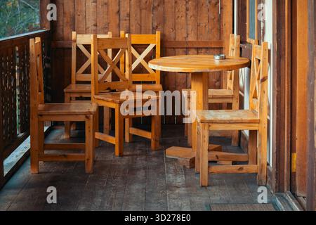 Eine hölzerne Terrasse mit einem runden Tisch und sechs Holzstühlen. Die Stühle sind um den Tisch herum angeordnet, und auf dem Tisch befindet sich eine Tasse. Konzept des rel Stockfoto