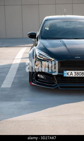 Rechte Vorderseite des Ford Focus auf dem Parkplatz. Der vordere Teil des schwarzen Fließhecks auf einer Straße, die helle Sonne wirft lange Schatten. Stockfoto