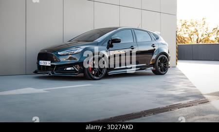 Schwarzer Ford Focus vor der beigefarbenen Gebäudewand. Dreiviertelansicht der sportlich modifizierten Ford-Fließheck. Stockfoto