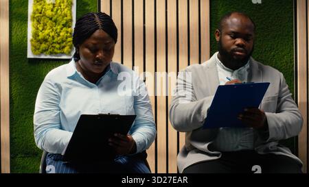 afroamerikanische Bewerber füllen Anmeldeformulare für Bewerbungsgespräche und offene Stellen aus, um eine erfolgreiche Rekrutierung und ein Treffen mit der Personalabteilung zu gewährleisten. Qualifikationen notieren. Stockfoto