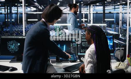 Multiethnisches Team in diversen Data Center-Codierungen mit generativer KI-Unterstützung. Der asiatische Mann überwacht die Arbeit eines IT-Experten, der künstliche Intelligenz nutzt großes Sprachmodell, Kamera A Stockfoto