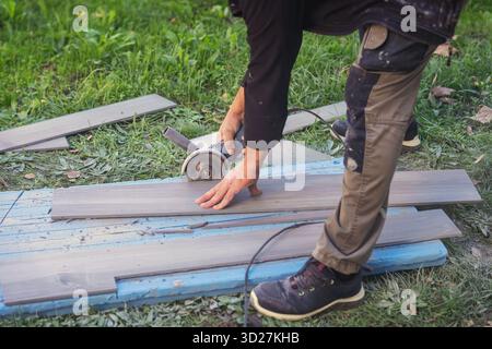 Arbeiter Schneidet Fliesen Im Freien. Bauarbeiter schneidet Fliesen mit einem elektrischen Schleifgerät auf dem Grasfeld während des Renovierungsprojekts im Freien. Konzept von Stockfoto