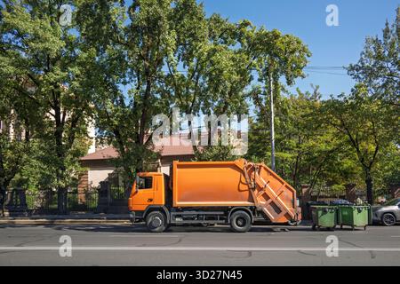 Jerewan, Armenien 10.16.2025. Ein großer orangener Müllwagen parkt am Straßenrand neben einem grünen Mülleimer Stockfoto