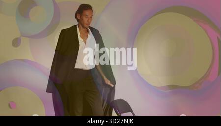 Stehendes männliches Model mit schwarzem Blazer und offenem weißem Hemd im Studio, mit projizierten Lichtringen Stockfoto