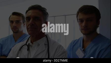 Stehender Oberarzt und zwei Ärzte mit Peelings und Abzeichen im Klinikkorridor, mit Jalousien Stockfoto