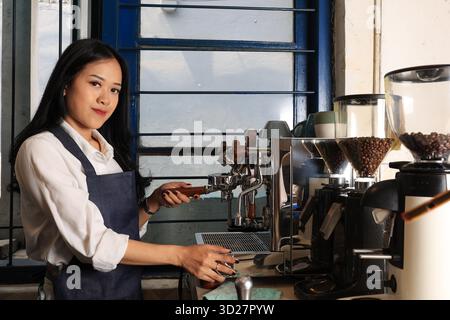 Weibliche Barista bereiten die Zubereitung von Kaffee mit der Espresso-Maschine in einem rustikalen asiatischen Coffeeshop vor Stockfoto