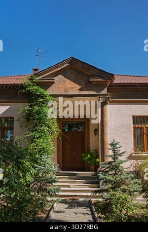 Ein Haus mit einer braunen Tür und einer grünen Efeupflanze, die an der Seite wächst. Das Haus hat eine große Eingangstür und ein kleines Fenster an der Seite Stockfoto