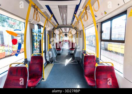 Geräumiges Interieur der modernen Straßenbahn Pesa 120Na „Swing“ in Warschau, Polen, mit grauem Boden, roten Sitzen und verschiedenen gelben Elementen. Stockfoto