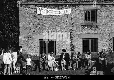 Dieses Schwarzweiß-Foto zeigt eine Szene während des jährlichen Well Dressing-Events in Chesterfield, Großbritannien. Eine Gruppe von Menschen versammelt sich draußen vor einem Steingebäude, mit einem Banner oben sichtbar. Das Bild zeigt ein öffentliches Ereignis, bei dem traditionelle Verfahren zum Well Dressing gezeigt werden. Stockfoto