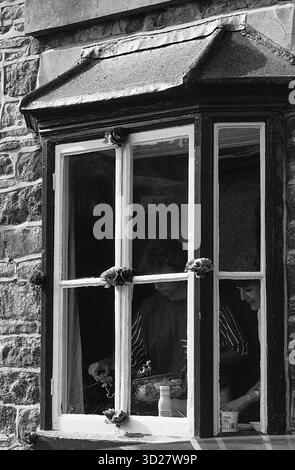 Dieses Schwarzweiß-Foto zeigt ein Fenster, das von dunkler Steinarchitektur eingerahmt ist. Das Fenster ist Teil eines Gebäudes, das während des Annual Well Dressing in Chesterfield, Großbritannien, dekoriert wurde. Das Bild fängt einen Moment des historischen und traditionellen Ereignisses ein. Stockfoto