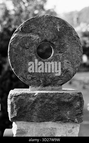 Dieses Graustufenbild zeigt eine Steinskulptur. Die Skulptur besteht aus einem großen, kreisförmigen Stein mit einem zentralen Loch, das auf einem kleineren, rechteckigen Steinsockel montiert ist. Das Bild wurde während der jährlichen Well Dressing-Veranstaltung in Chesterfield, Großbritannien, aufgenommen, einer traditionellen Feier, bei der Brunnen mit aufwendigen Schnitzereien dekoriert wurden. Stockfoto