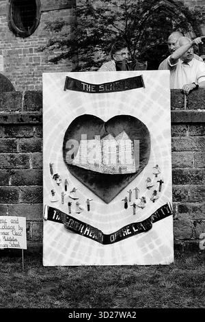 Das Bild zeigt ein großes, herzförmiges Banner, das im Rahmen des Annual Well Dressing in Chesterfield, Großbritannien, erstellt wurde. Das Banner zeigt eine Miniaturdarstellung von Chesterfield Castle und zahlreiche kleinere dekorative Elemente. Mehrere Personen sind im Hintergrund sichtbar und beobachten das Kunstwerk. Stockfoto